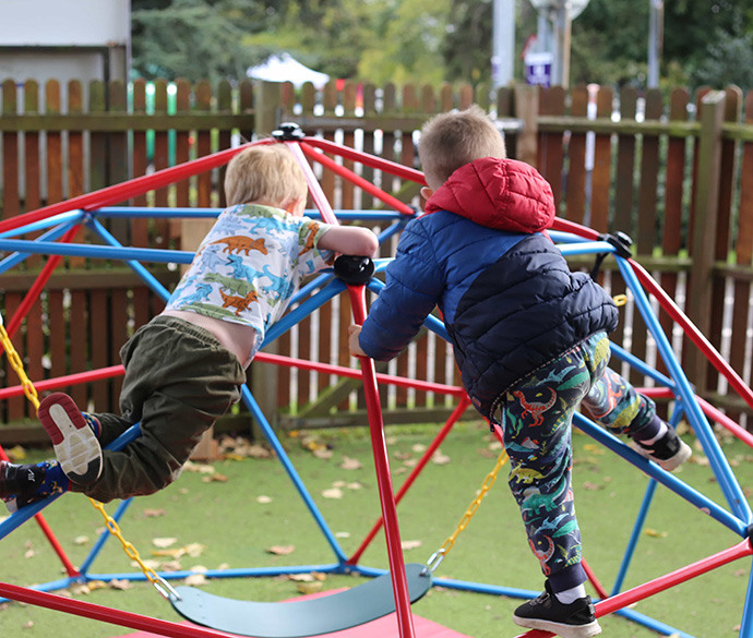Two children are playing on a colourful climbing structure in an outdoor playground.