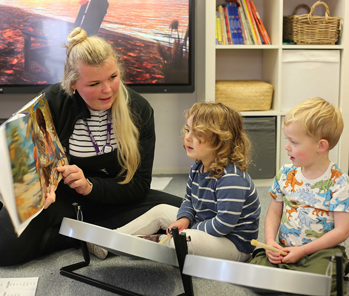 An adult is reading a storybook to two young children in a classroom setting.
